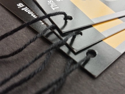 Folded tags on glossy stock with black, gray, and yellow color fields strung with standard black rayon string.