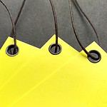 Tags of yellow cover stock reinforced with our black eyelets and strung with our black waxed cord.