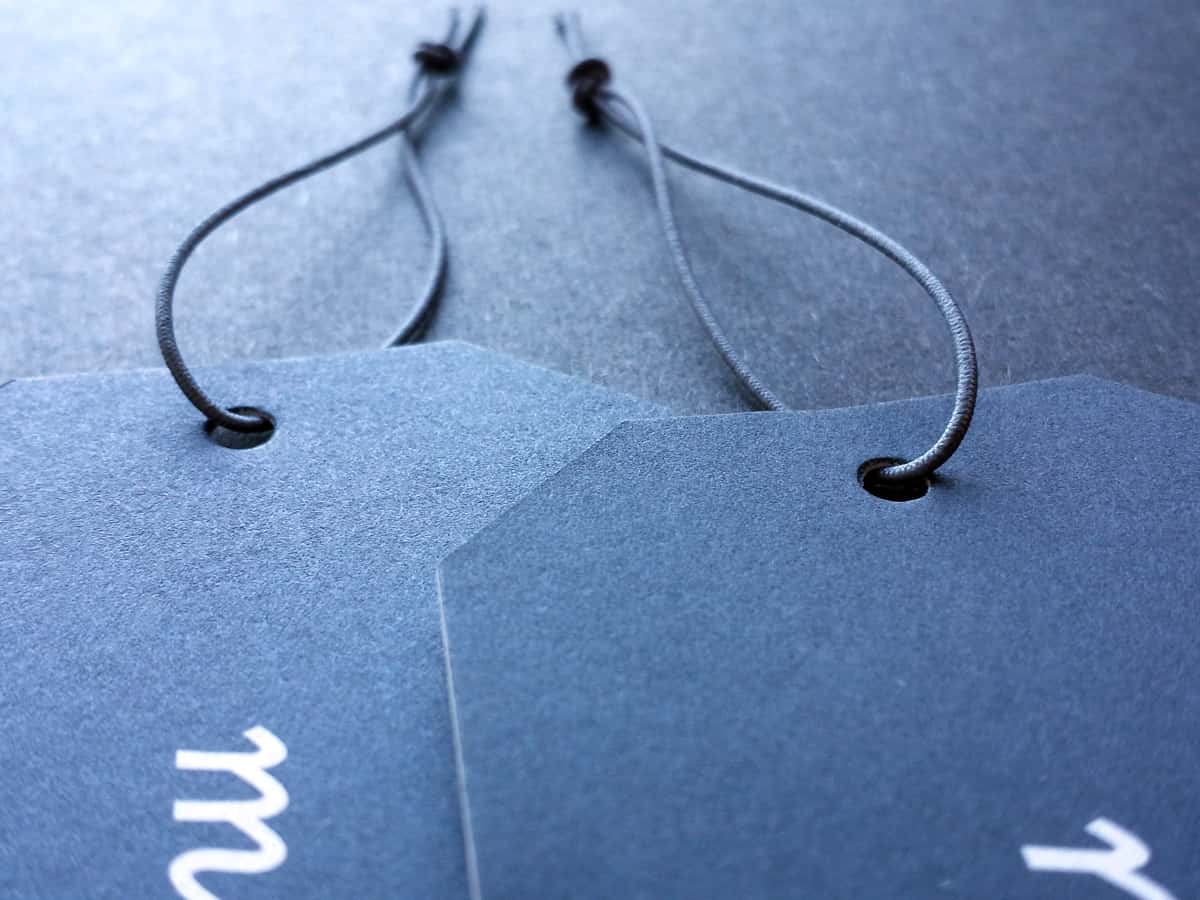An image of two die-cut tags of heavy paper stock, strung with dark navy blue elastic, on a charcoal gray background.