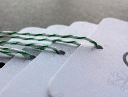 Tags with rounded corners and foliage graphic strung with green bakery twine.