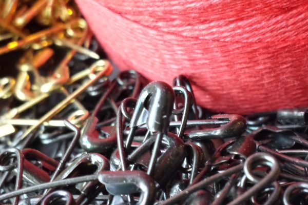 handwork-featured Photograph of hand assembly components, including red waxed cord, and safety pins typically used for application to garment tags.