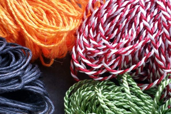 Photograph of bundles of knotted loops; from top left: dark orange mercerized cotton, red-white variegated Pearlray, leaf green heavyweight Pearlray, and black waxed cord.