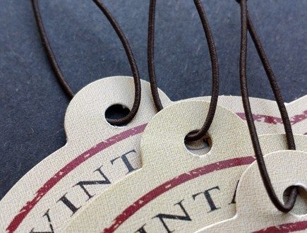 Tan die-cut tags with a maroon border strung with brown non-fray elastic.