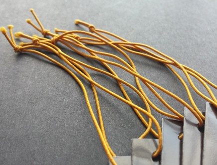 Dark brown tags strung with gold non-fray elastic.
