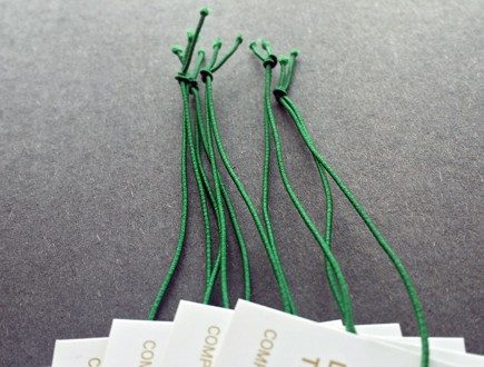 White tags with gold copy strung with green non-fray elastic.