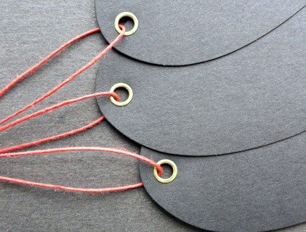 Ovular black tags with brass eyelets strung with red waxed cord.
