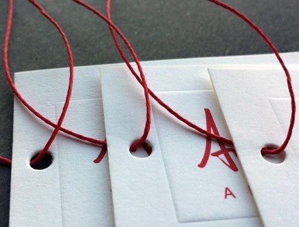 Tags with debossed border, strung with red waxed cord.