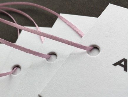 Tags on heavy white cover stock with black copy strung with light pink 1/16